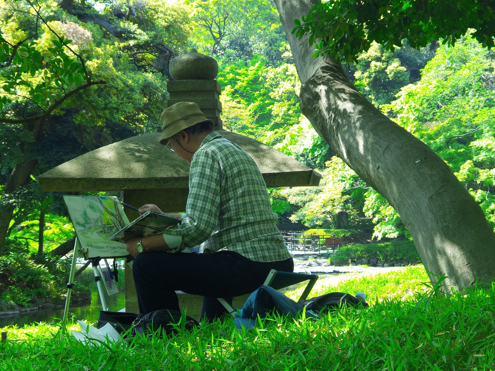 Artist perched under the shade of green trees Painting the Landscape