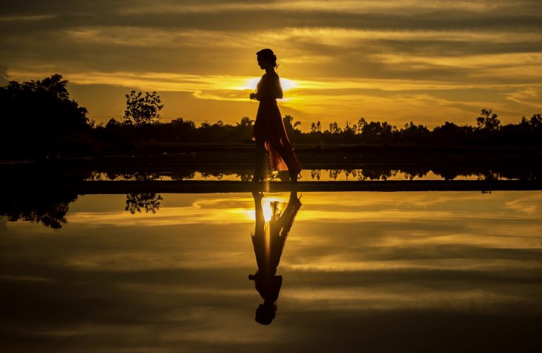 Woman walking near water at sunset